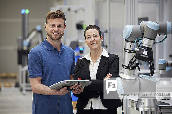 Confident manager and technician standing next to machine in industry
