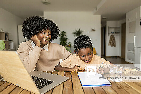 Happy mother with son writing on note pad and studying at home