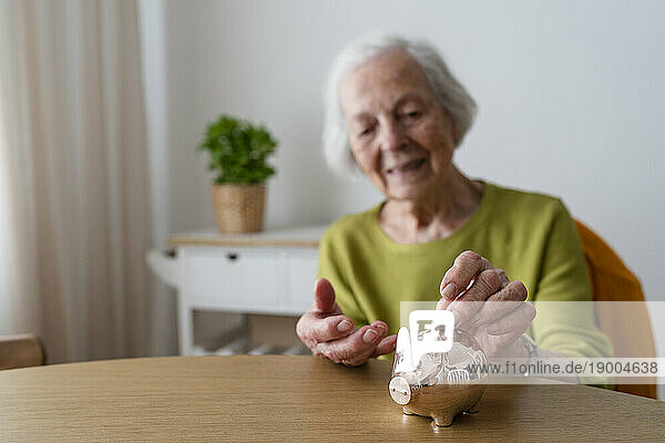 Senior woman putting coin in piggy bank on table