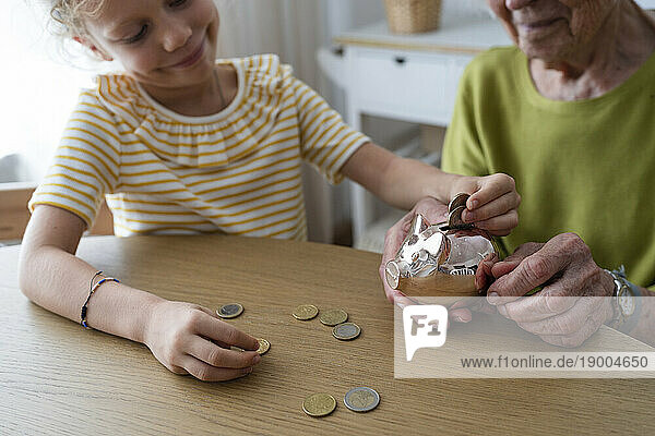 Smiling granddaughter putting coin in piggy bank