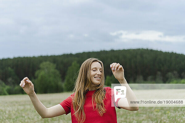 Smiling young woman in red t-shirt dancing on field