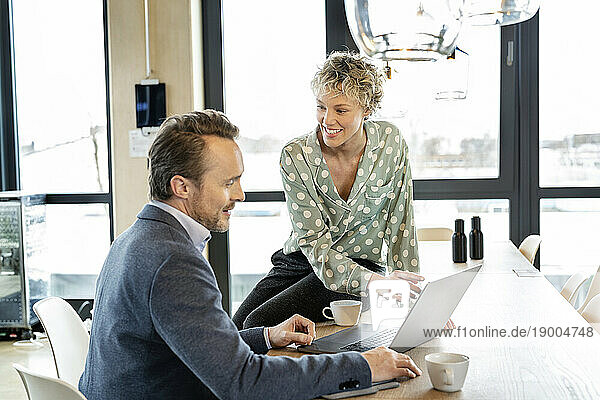 Smiling businesswoman and businessman discussing over laptop