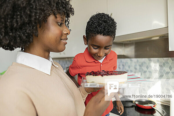 Smiling boy with mother holding cake in kitchen at home
