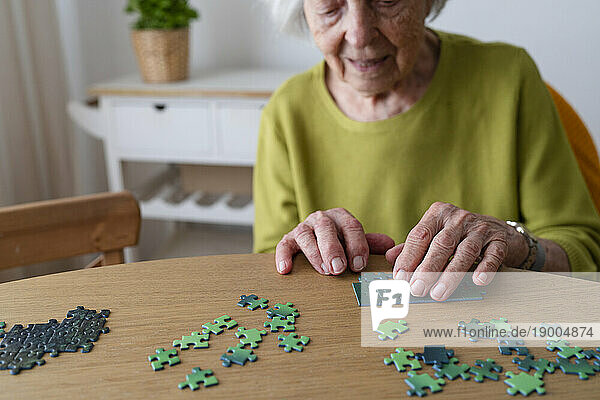 Senior woman solving jigsaw puzzle on table at home
