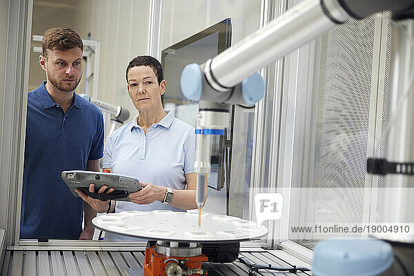 Colleagues examining robotic arm using equipment in industry