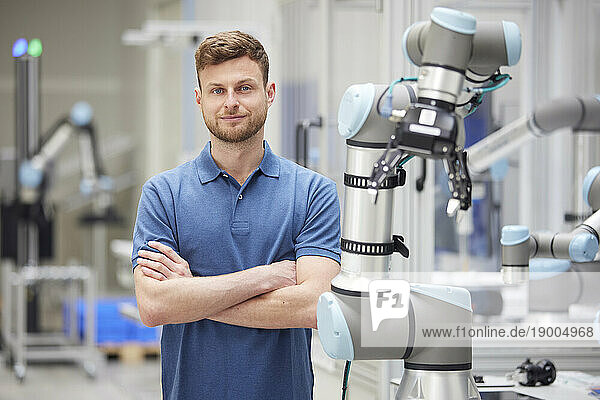 Confident technician with arms crossed standing next to machine in industry