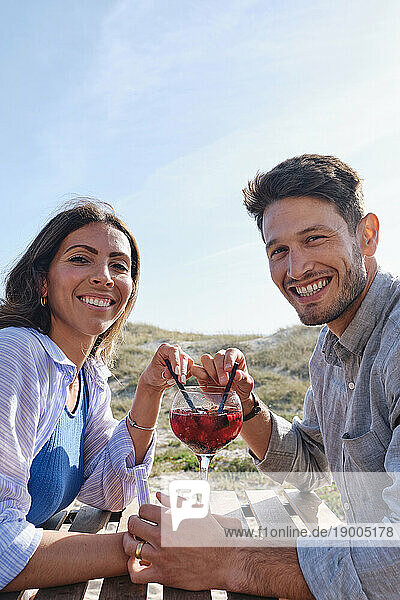 Happy couple enjoying drink at table on beach
