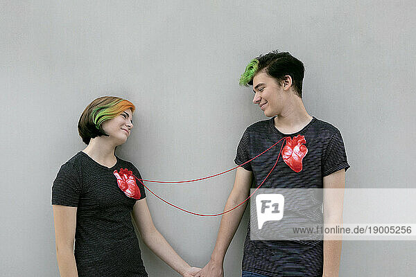 Teenage couple connected with hearts in front of gray background