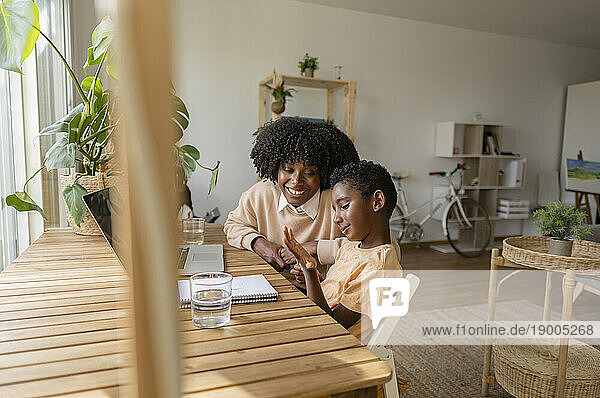 Happy woman with son sitting at wooden table in living room