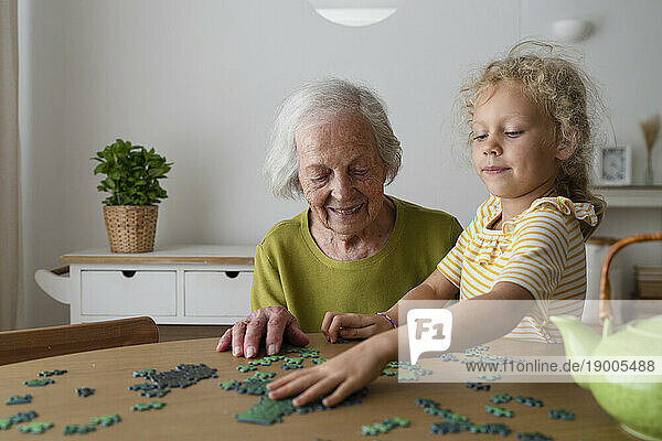 Grandmother and granddaughter solving jigsaw puzzle on table