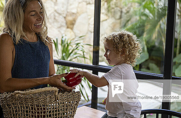Happy woman giving red bell pepper to son at home