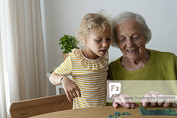 Grandmother teaching granddaughter to solve jigsaw puzzle at home