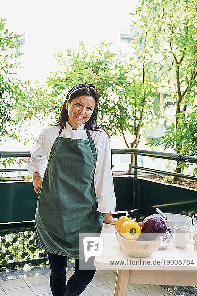 Smiling chef wearing apron leaning on table in balcony