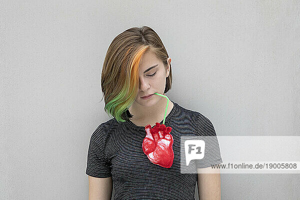 Teenage girl with dyed hair drinking from heart against gray background