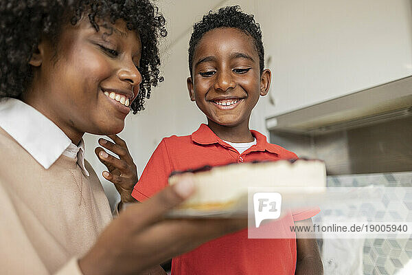 Happy boy with mother holding cake in kitchen at home