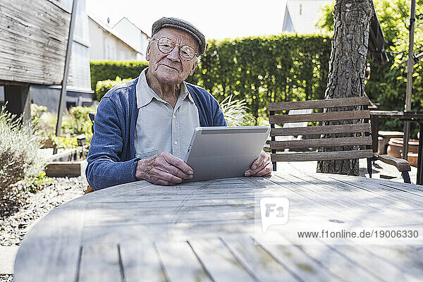 Smiling senior man sitting with tablet PC at table