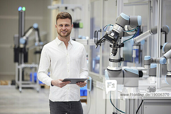 Smiling technician holding tablet PC next to machine in industry