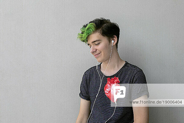 Teenage boy listening heartbeat with headphones connected to heart against gray background