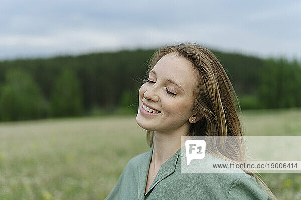 Smiling young woman with eyes closed on field