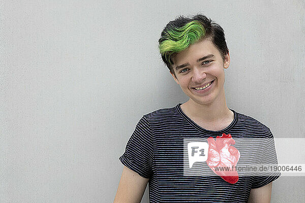 Smiling teenage boy with dyed green hair and artificial heart against gray background