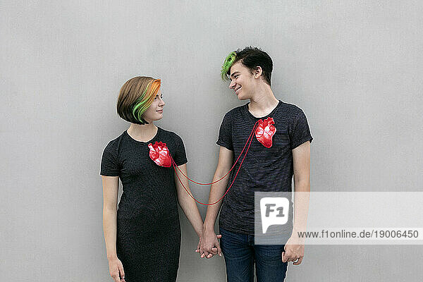 Teenage couple connected with hearts and holding hands against gray background