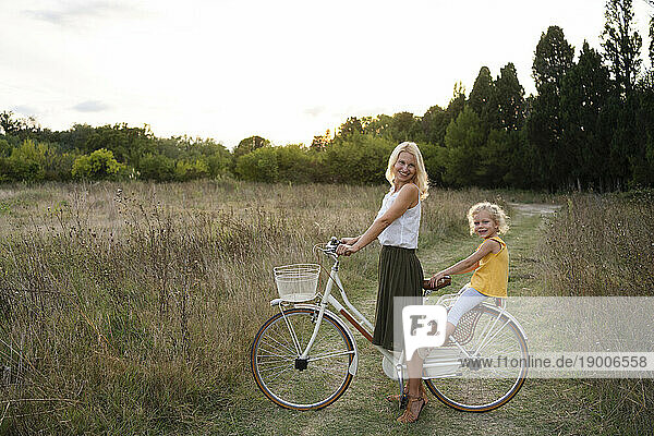 Happy mother with daughter sitting on bicycle at sunset