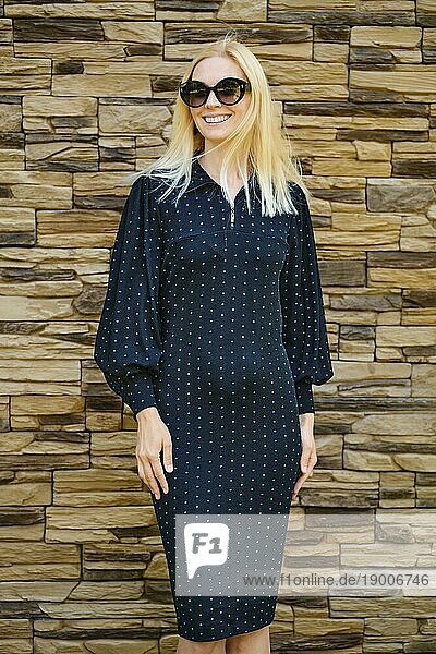 Mittleres Nahaufnahmeporträt einer lächelnden Frau in schwarzem Kleid mit Punktmuster