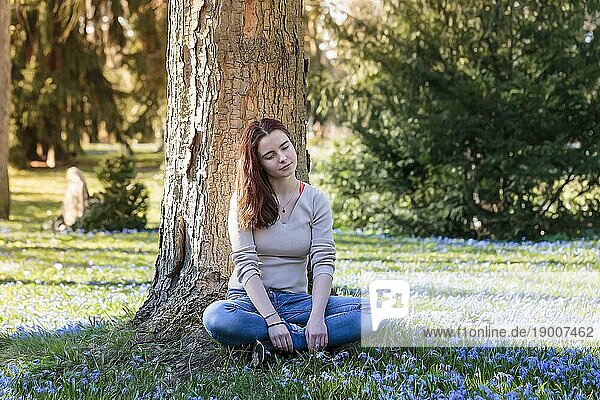 Verträumte junge Frau sitzt auf einer Blumenwiese