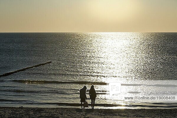 Sonnenuntergang über dem Meer mit zwei Personen am Strand