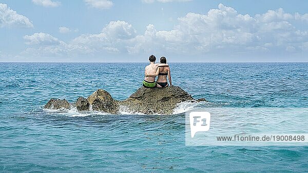 Junges Paar sitzt auf einer Klippe in der Mitte des Meeres