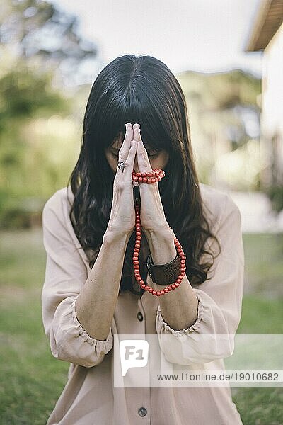 Eine achtsame Frau hält ihre Hände in der Namaste Position  während sie auf ihrem Hinterhof die Atmung übt
