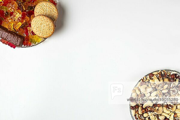 Gegenüberstellung ungesund und gesund  verschiedene Süßigkeiten und Nüsse  auf Tellern  weißer Hintergrund  Kopierraum