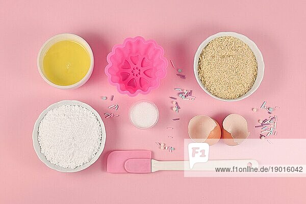 Backzutaten und Werkzeuge wie Puderzucker  gemahlene Mandeln  Eiweiß  Salz  Zuckerstreusel und Kuchenform auf rosa Hintergrund