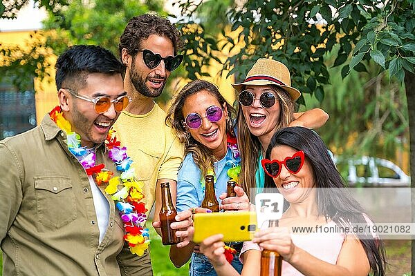 Multiethnische Gruppe von Freunden  die im Stadtpark feiern und ein Selfie machen  lächelnd beim Betrachten der Fotos auf dem Handy