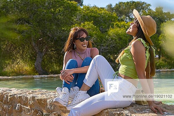 Weibliche Freunde haben Spaß im Urlaub in einem Park im Sommer  sitzen lächelnd an einem See