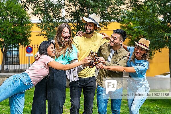 Eine multiethnische Gruppe von Freunden feiert in einem Stadtpark und stößt mit Bierflaschen an