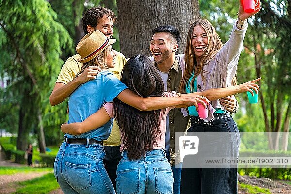Multiethnische Gruppe von Geburtstagsfeier in der Stadt Park umarmt in einem Symbol der Freundschaft für immer und lächelnd eine Menge