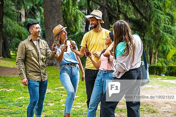 Eine multiethnische Gruppe von Freunden feiert in einem Stadtpark mit Bierflaschen