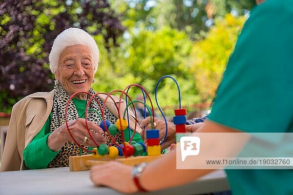 Hand einer älteren Frau im Garten eines Pflegeheims oder Seniorenheims  die mit Spielen zur Verbesserung der Beweglichkeit der Hände spielt  lächelnd
