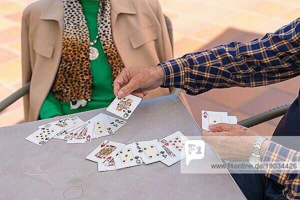 Hände zweier älterer Menschen im Garten eines Pflegeheims oder Seniorenheims  die an einem Sommermorgen Karten spielen