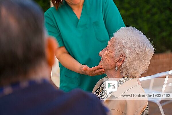 Eine ältere oder reife Frau mit der Krankenschwester im Garten eines Pflegeheims in einem Moment der Liebe und Zuneigung streichelt das Gesicht