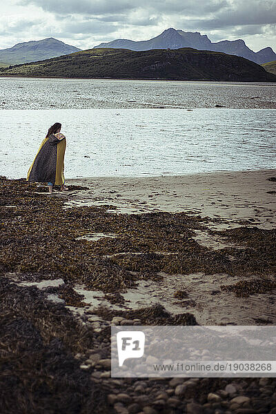Woman in long cloak walking on beach in Scotland
