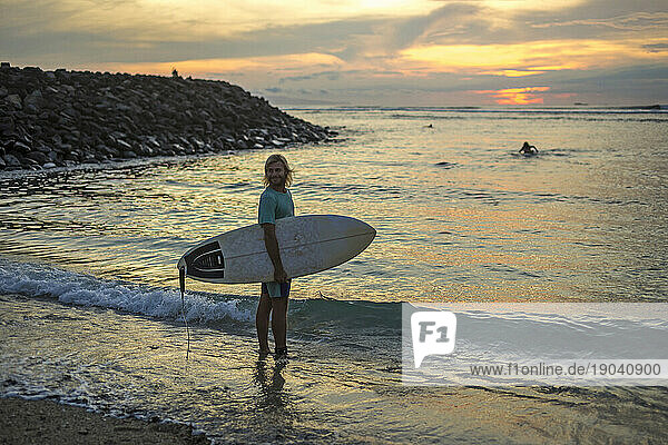 A Surfer stands in ankle-deep water at sunset
