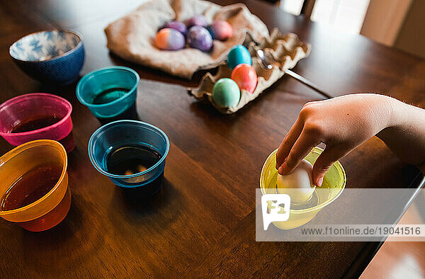 Hand dipping an egg in container of dye to make colorful Easter egg.