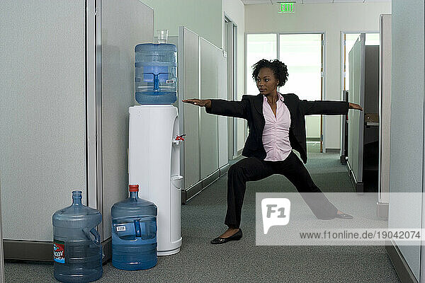 Executive woman does yoga by the water cooler while at work in Santa Clara  California.