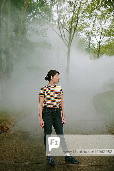 Young woman standing on a foggy path in a park looking away