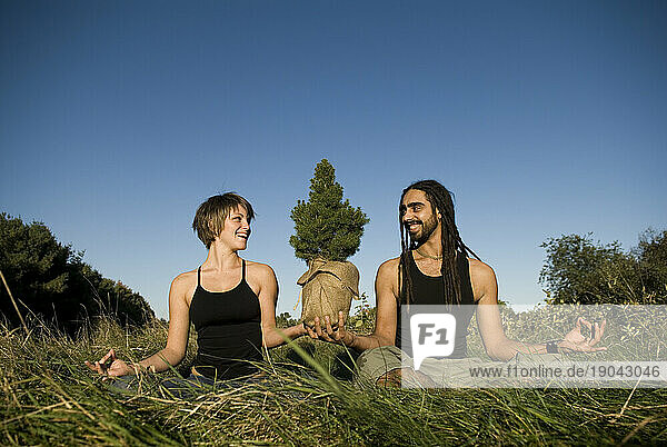 A man and woman doing yoga while together holding a tree  Maine.
