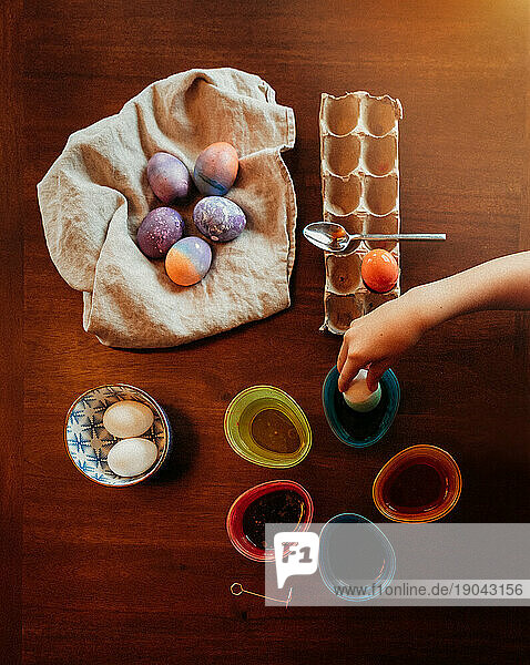 High angle shot of child's hand dipping egg in dye to make Easter egg.