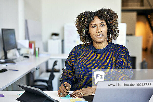 Thoughtful businesswoman with adhesive notes on desk standing in office