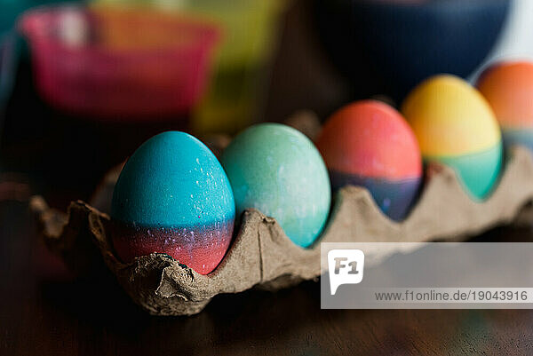 Row of brightly dyed Easter eggs in a carton on a table.